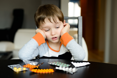 worried 4 year old boy sitting at the table with medications at home